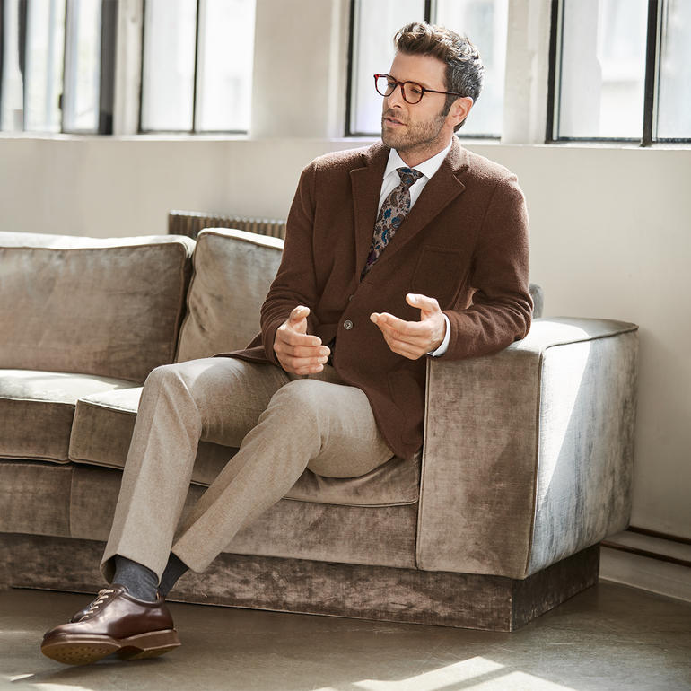 Ascot tweed-stropdas met bloemenprint Man draagt een bruine blazer met een gestreept stropdas patroon, zittend op een bank.