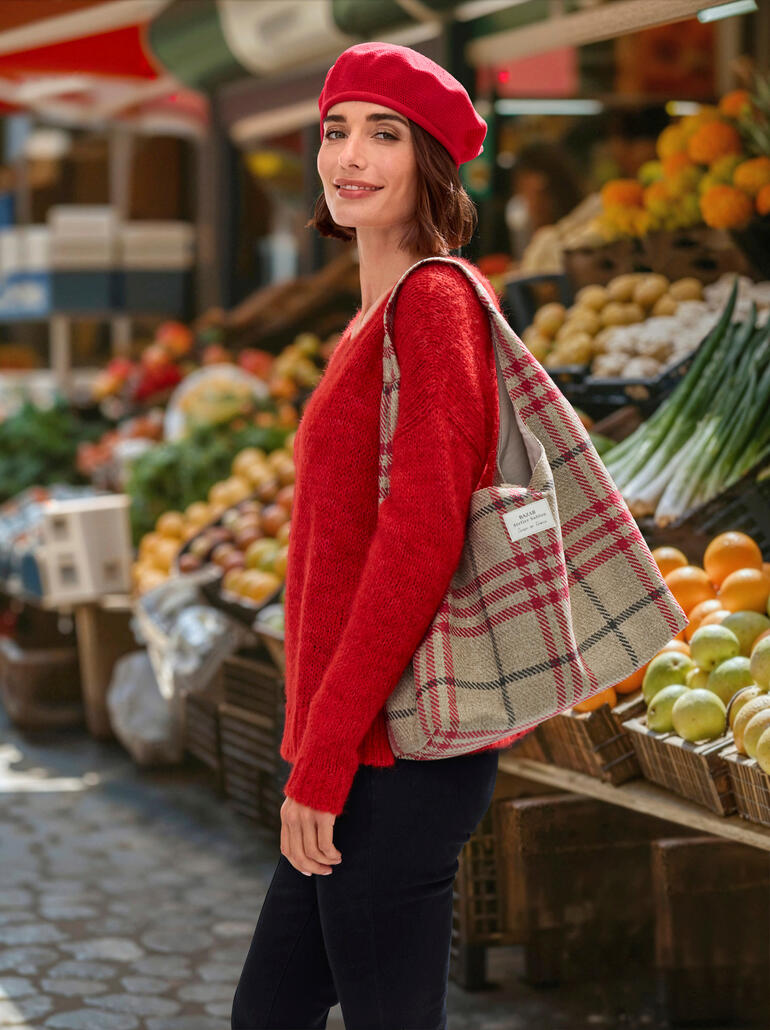 Vrouw draagt een rode katoen baret en een rode trui, staat op een markt.