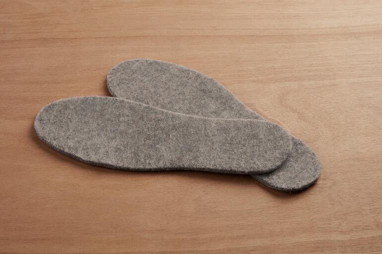 Twee grijze alpaca thermische schoen-inzetten op een houten ondergrond.