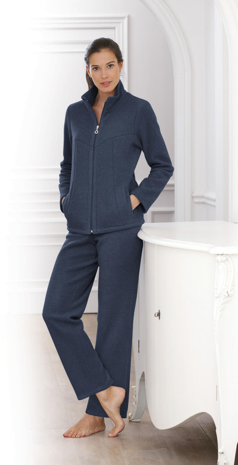 Vrouw in een marineblauw fleece-homesuit met ritssluiting en open zakken.