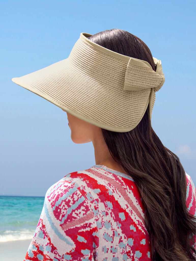 Vrouw met papieren hoed kijkt zijwaarts naar het strand.