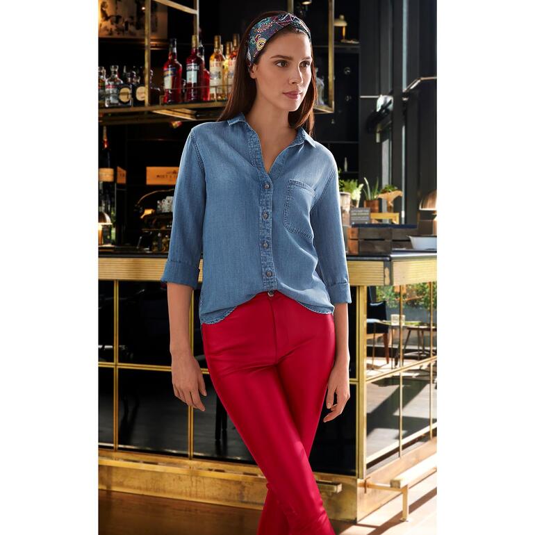 Een vrouw in een blauwe jeansblouse en rode leggings staat naast een bar.