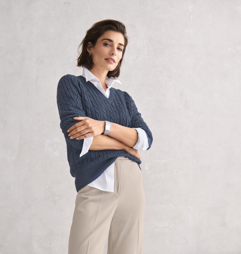 blauw Vrouw poseert in een grijze Carbery linnen kabeltrui en beige broek.