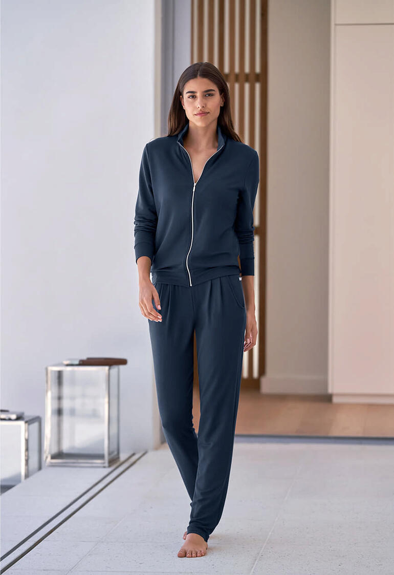 Vrouw in donkerblauwe modal huispak met rits loopt in een lichte ruimte.