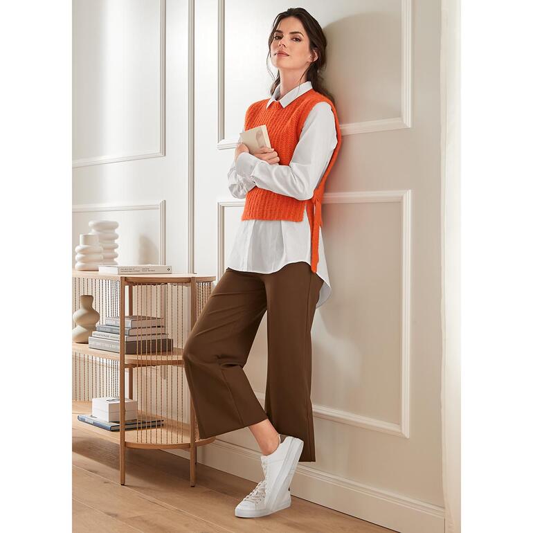 Modieuze bruine wijde broek met witte sneakers, gecombineerd met een oranje pullover.