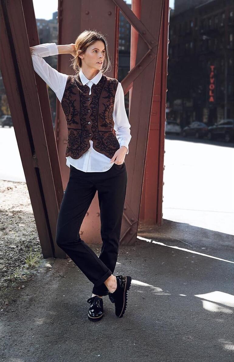 Vrouw in alpaca-ornament vest en zwarte broek, uitdagend poserend in de stad.