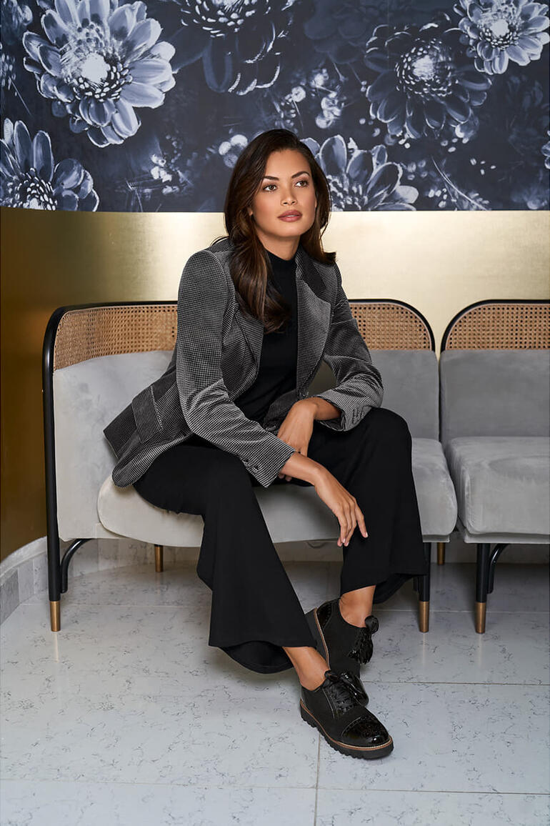 zwart/grijs Vrouw in een wasbare fluwelen blazer met houndstooth patroon op een bank.