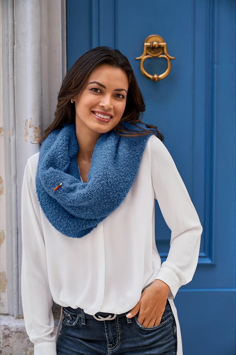 wit Vrouw draagt een witte blouse met een blauwe bouclé poncho voor een blauwe muur