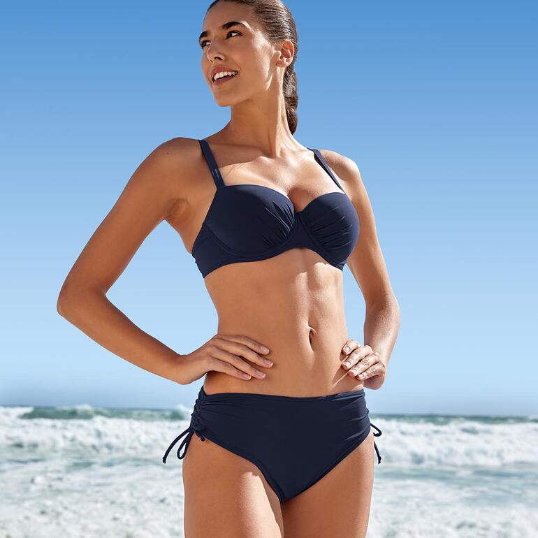 Donkerblauwe Sunflair® ReNew-bikini gedragen door een vrouw op het strand.