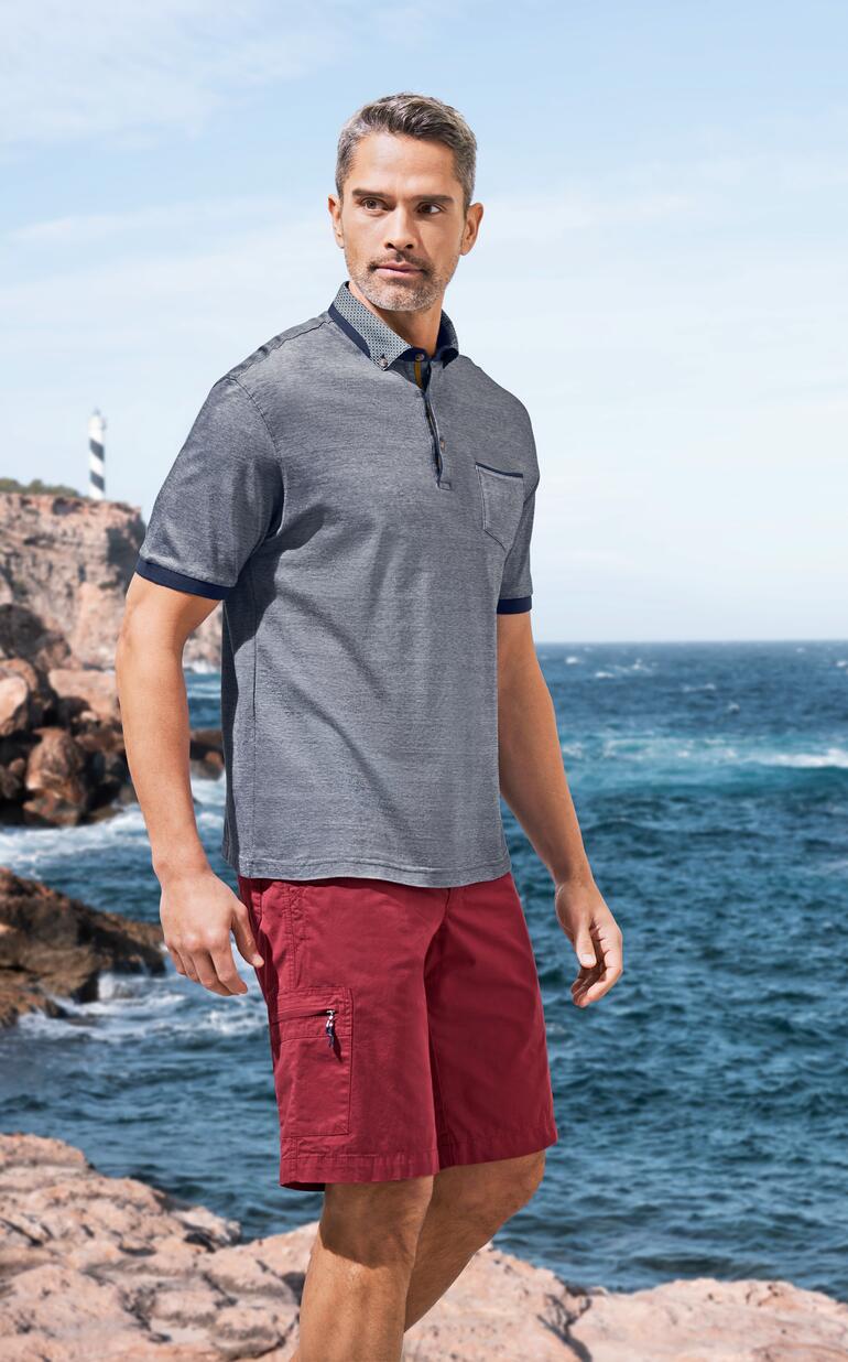 Man in polo en rode bermuda aan het strand.