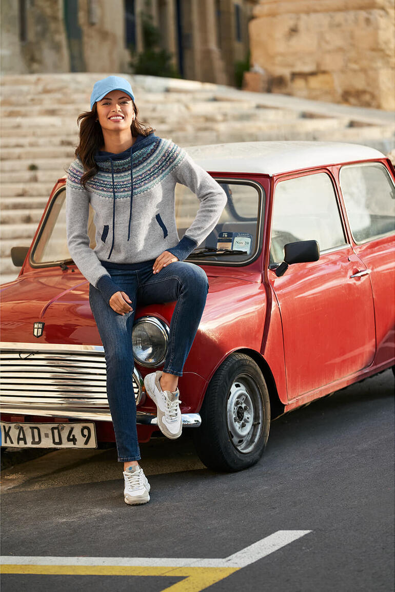 Vrouw zit op een rode auto met Satorisan vintage sneakers.