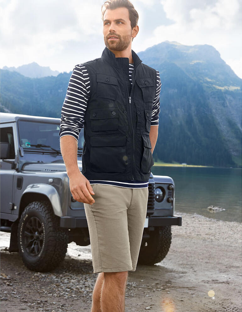 Man in zwart 10-pocket vest en gestreept shirt aan een bergmeer.