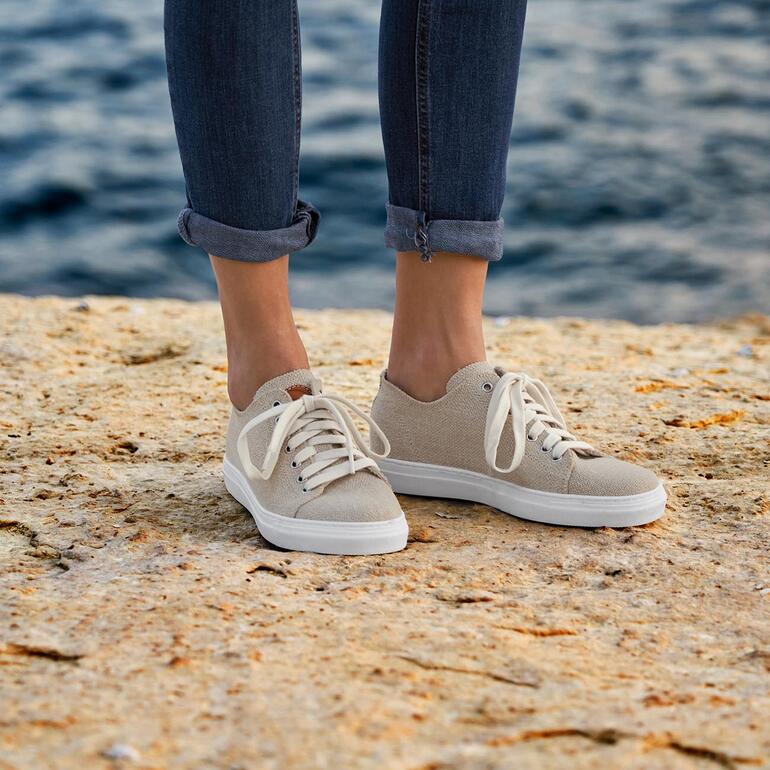 dames Beige Risorse Future hennep sneakers op voeten aan een kustlijn