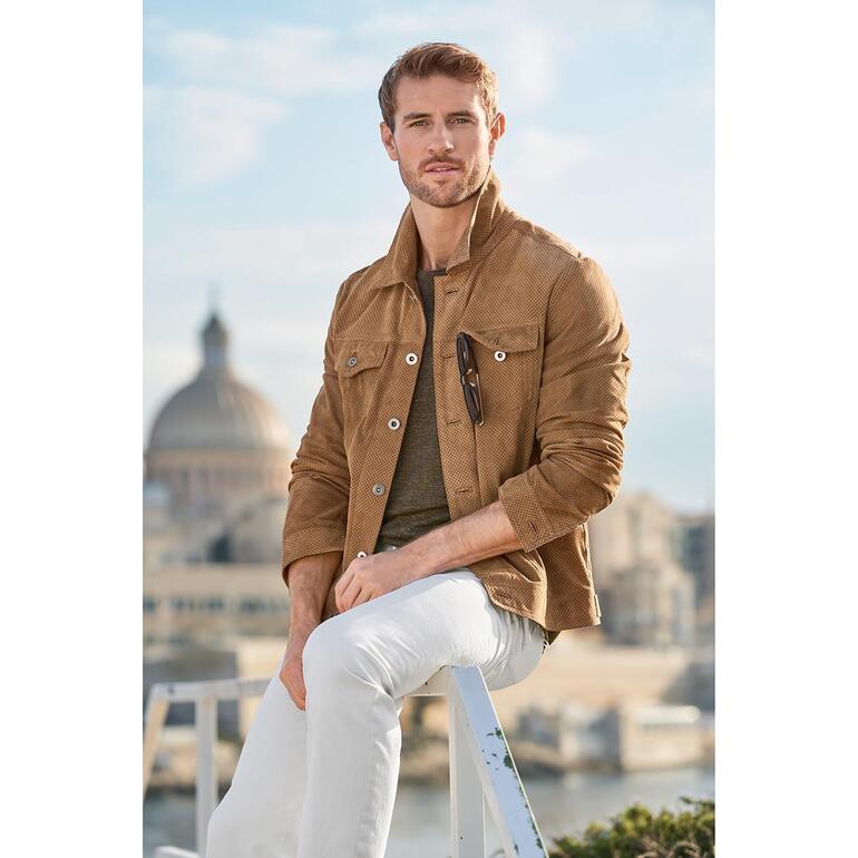 Man in geperforeerde leren jeansjack met witte broeken.