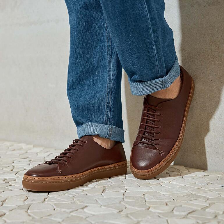 donkerbruin Man in bruine leren sneakers met jeans op een lichte vloer.