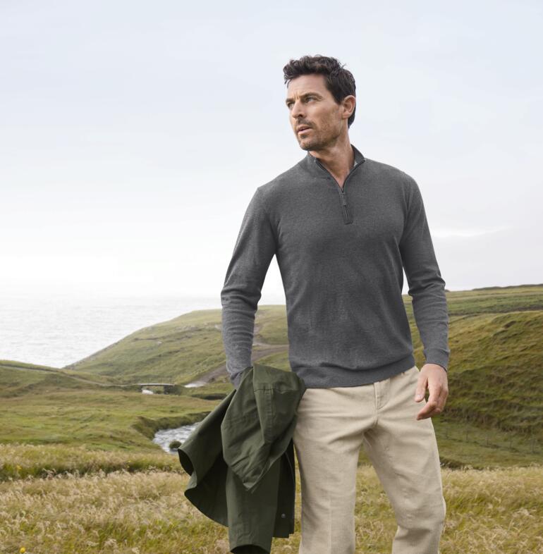 Man draagt een grijze Alan Paine all-season troyer met een omgeving op de achtergrond.