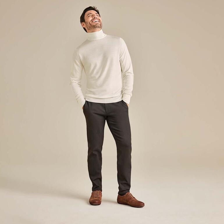 John Smedley coltrui Man in witte coltrui en grijze broek, lachend.