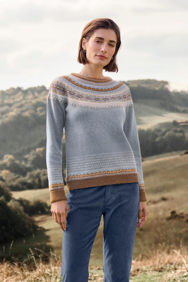 Vrouw in Fair-Isle-pullover staat glimlachend op een weiland.