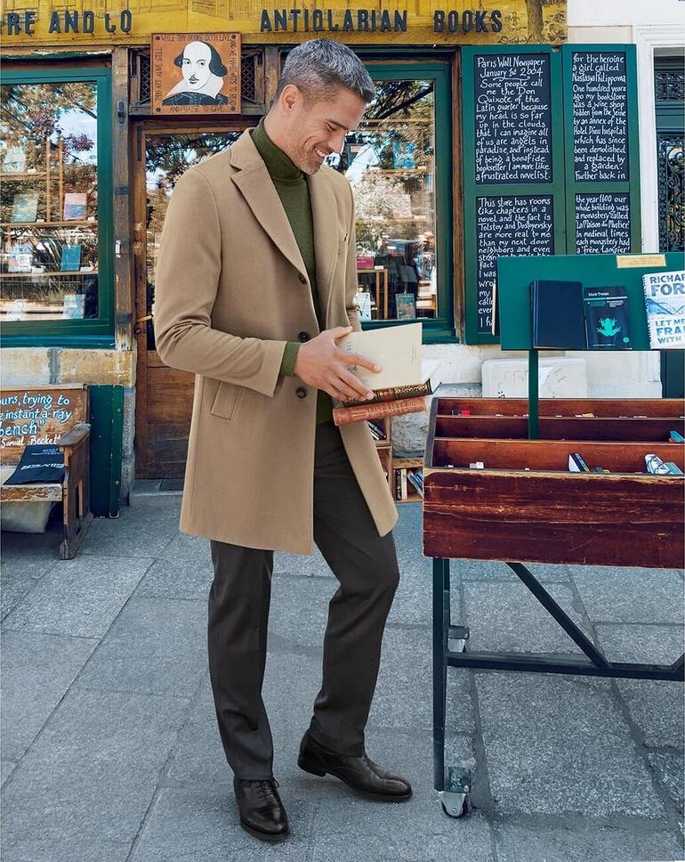Man in kasjmieren mantel in beige, staand voor een boekwinkel