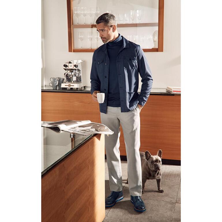 Man in navy hopsack wollen broek, staand in een moderne keuken.