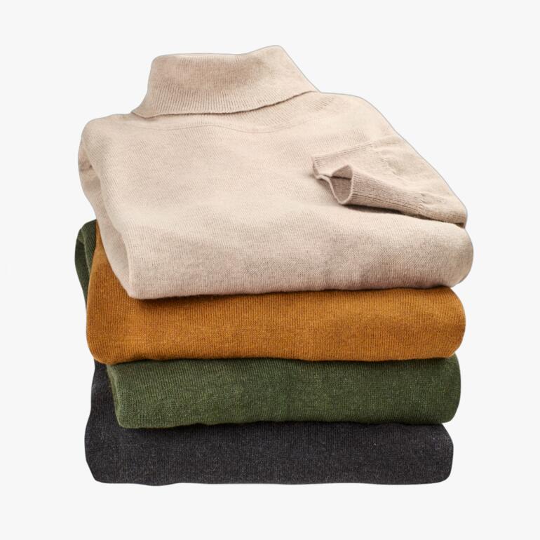 Stapeltje fijngebreide coltruien in verschillende kleuren.