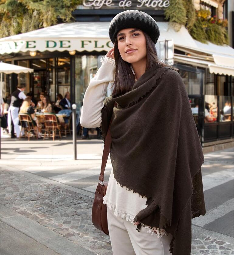 multi zwart/creme/grijs Close-up van een vrouw met een bruine poncho met franjes en een hoed.