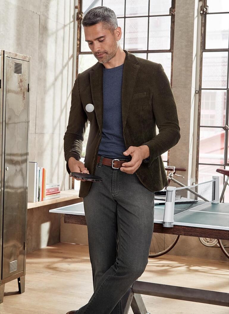 navy Man in blazer en T-shirt, kijkt naar een smartphone, naast een tafel met accessoires.