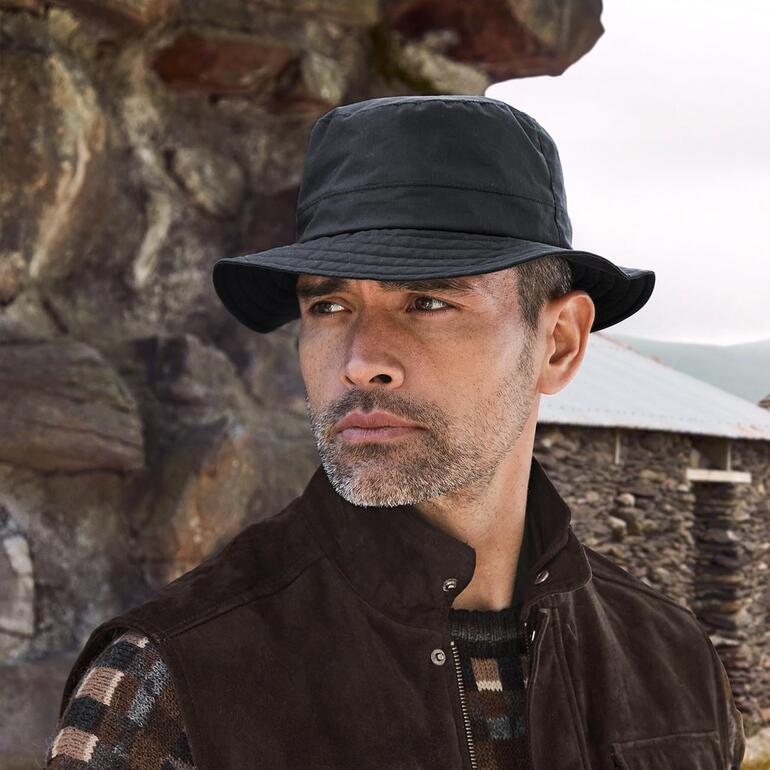 Mayser waxed cotton Man draagt een zwarte waterdichte hoed in de buitenlucht.