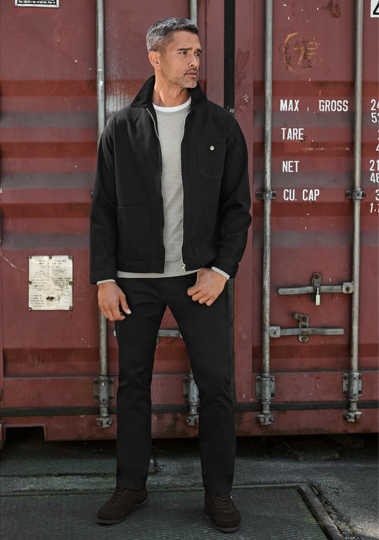 Edwin Selvage-jeansjack Man in een zwarte Edwin Selvage-spijkerjack staat voor een container.