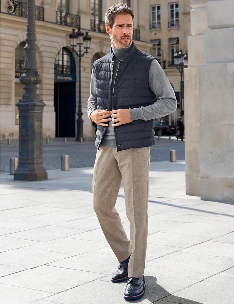 grijs Man in een grijze gewatteerde vest staat op een plein met elegante gebouwen.