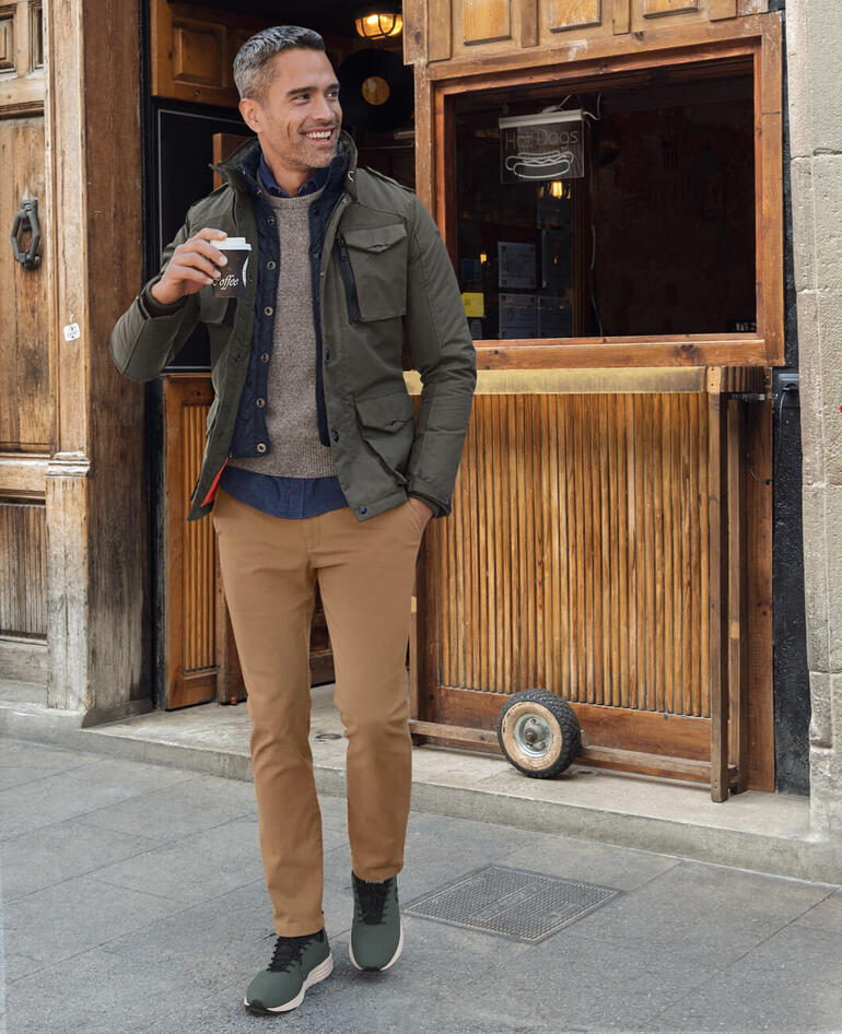 Jakpullover Man in duurzame sneakers, drinkt een koffie.
