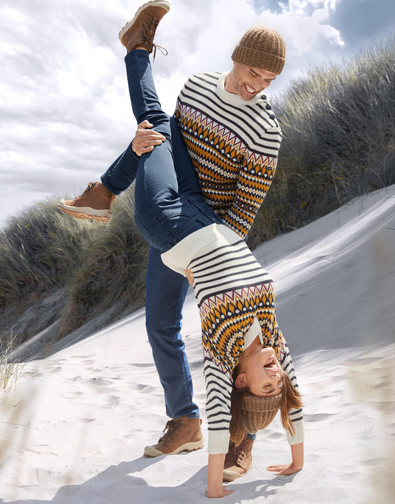 heren en dames Man tilt speels een vrouw boven het strand, beiden in jacquardtruien.