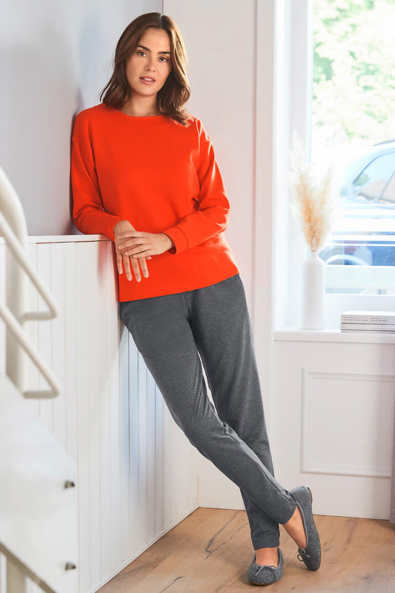 Gottstein walkballerina’s Vrouw in een rode sweatshirt en grijze joggingschoenen leunt tegen een trap.