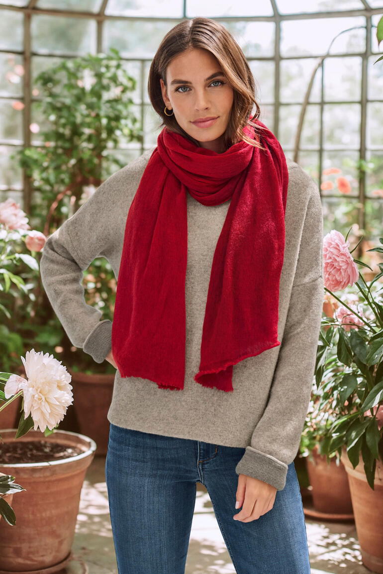 Vrouw draagt een rode cashmere sjaal in een tuin.