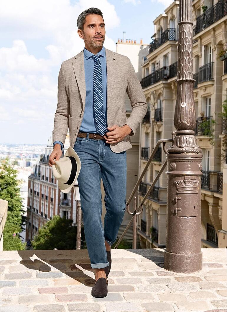donkerbruin Man in Supima piqué shirt, in een stedelijke omgeving met een blazer, gestreepte stropdas en hoed.