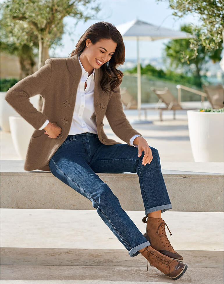 Vrouw in een bruine Softwalk-jack van Mirabell, ontspannen op een stenen bank.