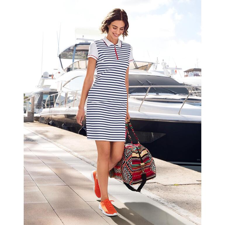 Vrouw in een gestreept polokleed van Saint James, loopt in de haven met tas.