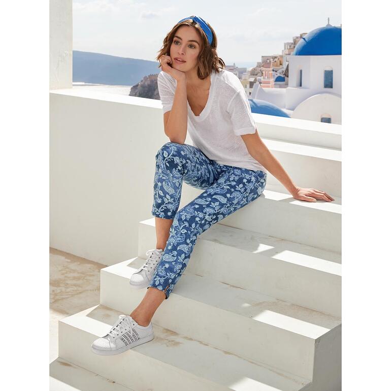 Vrouw zit op trappen in een blauwe paisley broek en een wit shirt.