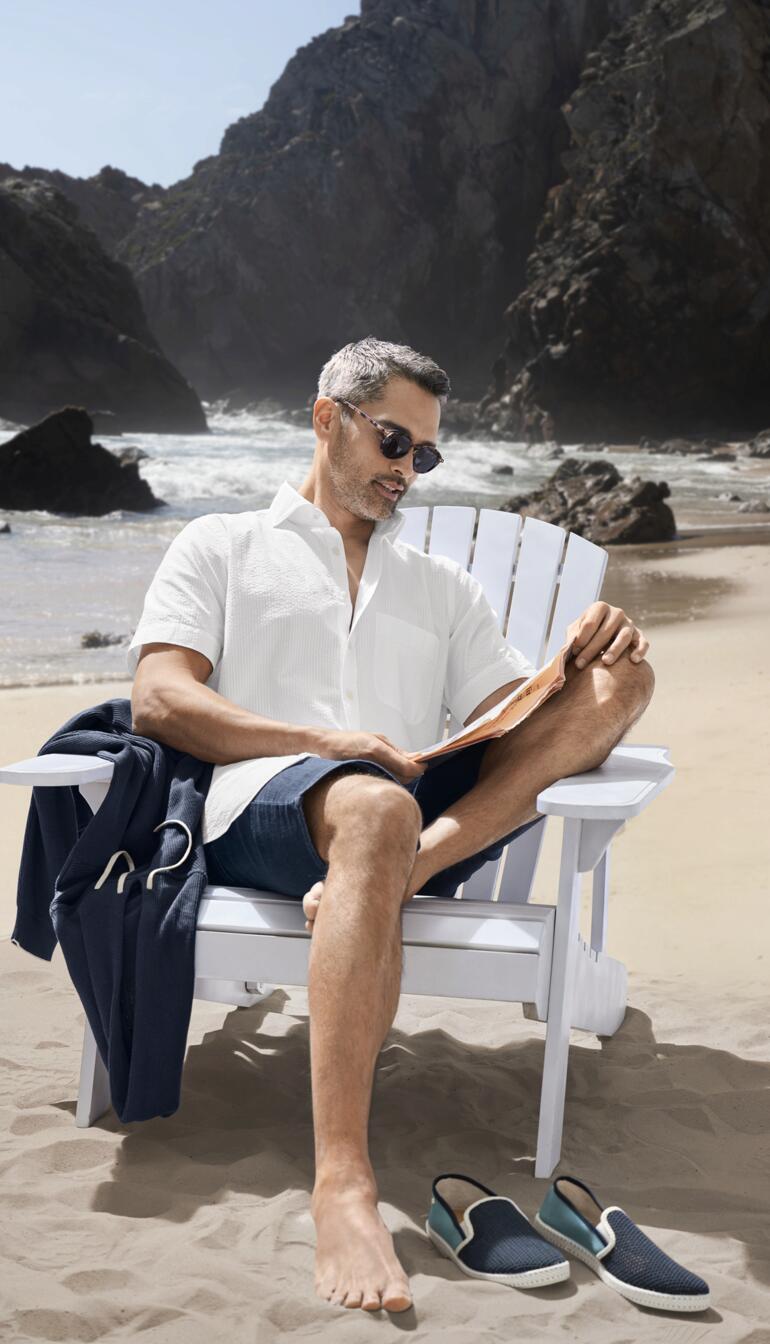 Man in seersucker overhemd zit relaxed op een stoel aan het strand.
