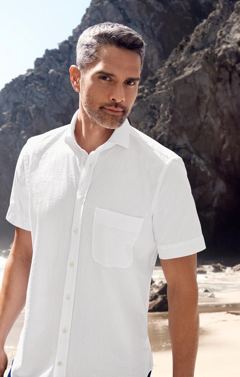 Man in wit seersucker overhemd buiten met rotsen op de achtergrond.