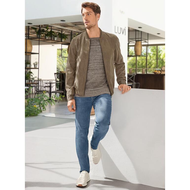 Man in Amaretta-blouson, staande tegen een muur in een moderne omgeving.