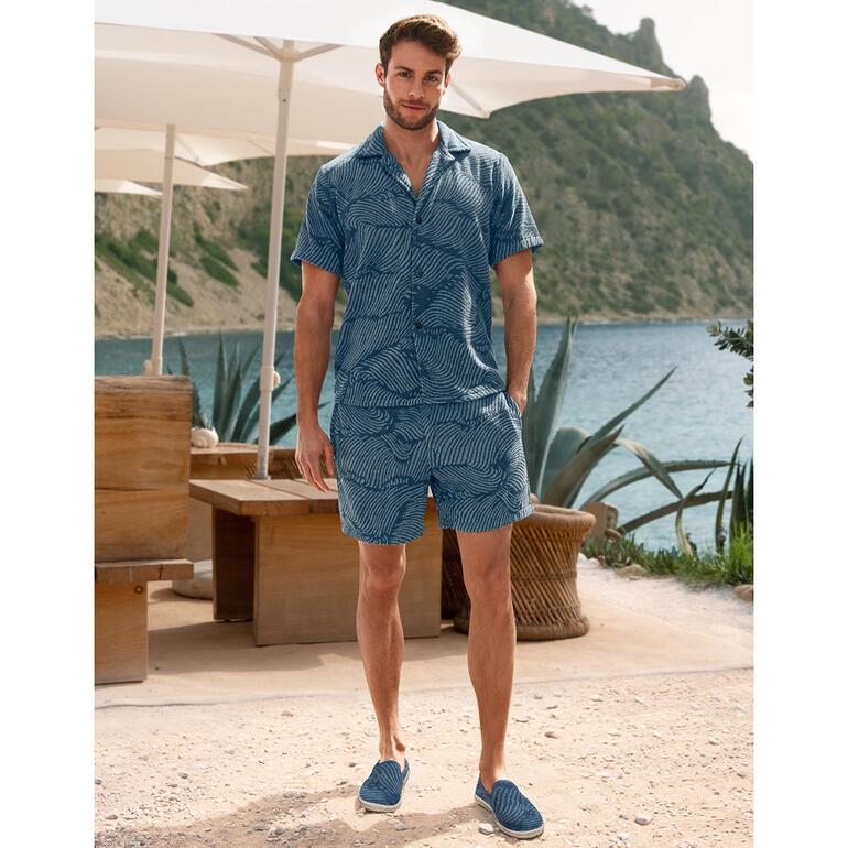 Man in gestreept Terry-shirt en korte broek staat op het strand