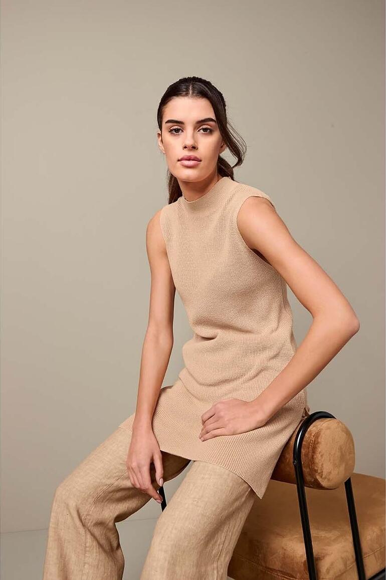 Junghans 1954 lange pullover in beige, model zit op een kruk.