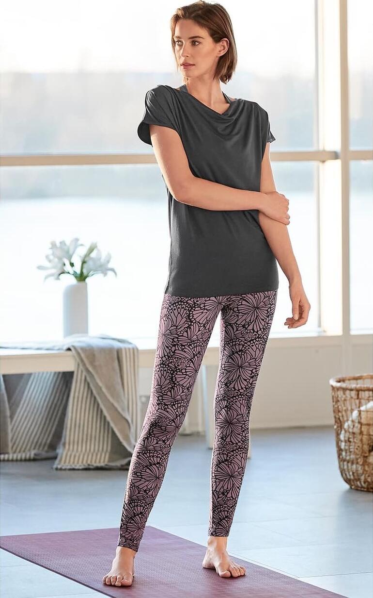 Vrouw in yoga watervalshirt en florale legging, staand op een yogamat