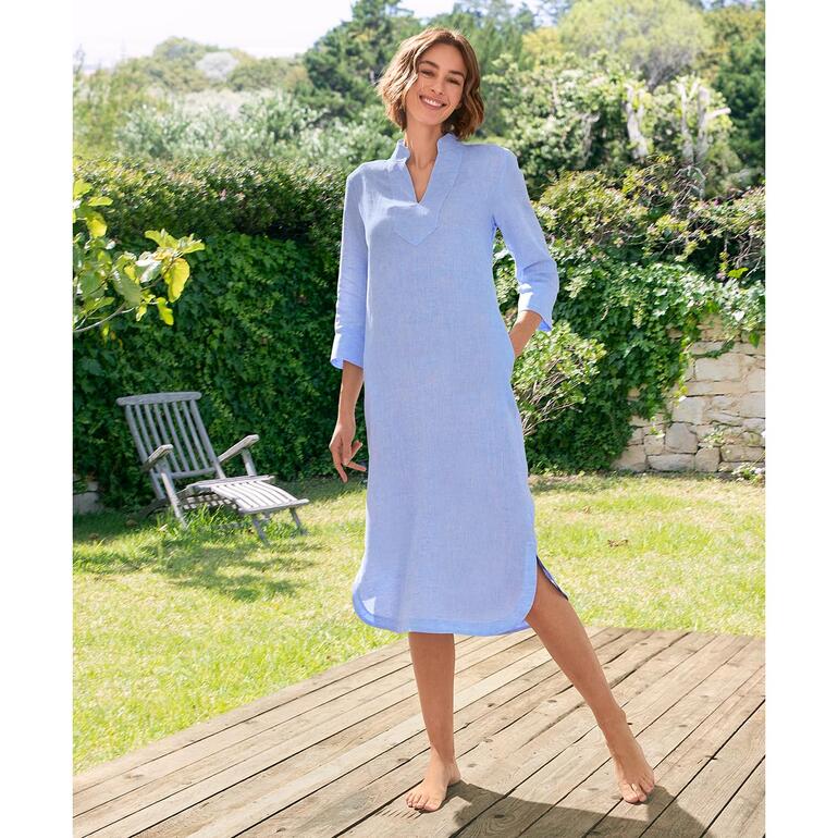 Vrouw in een blauwe linnen tuniekjurk, staat in de tuin