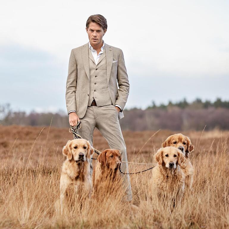 Man in soft donegal jasje met drie honden in de buitenlucht.