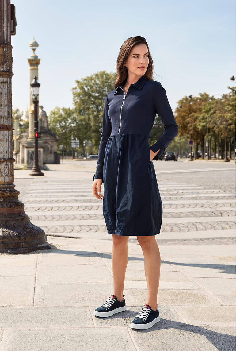 Vrouw in navy casual jurk op een straatcorner met historische gebouwen.