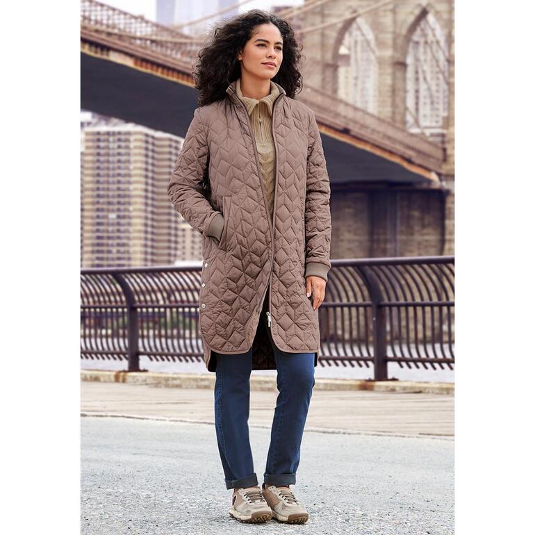 Satorisan duurzame sneakers Vrouw in duurzame sneakers en een bruine gewatteerde jas voor een brug in de stad.