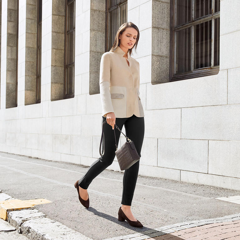 Vrouw in zwarte lange broek en beige top, loopt op straat.