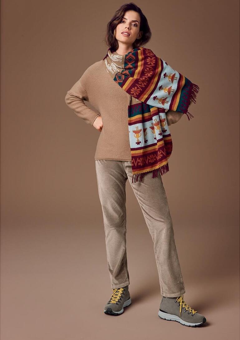 Vrouw draagt een handgebreide alpakashawl met een beige trui en joggingsbroek.